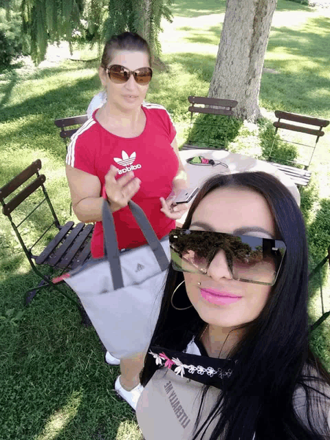 a woman wearing a red adidas shirt stands next to another woman wearing sunglasses