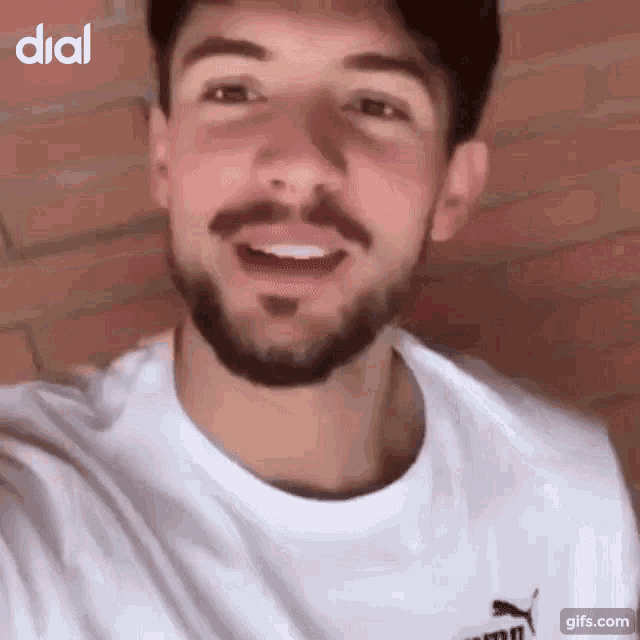 a man with a beard is wearing a white puma shirt and smiling .
