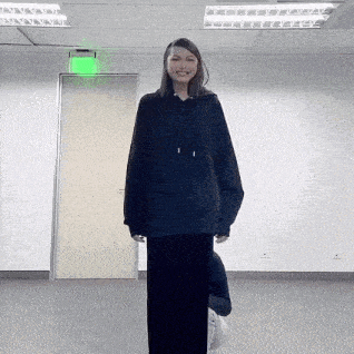 a woman wearing a black hoodie and a black skirt is standing in a room .