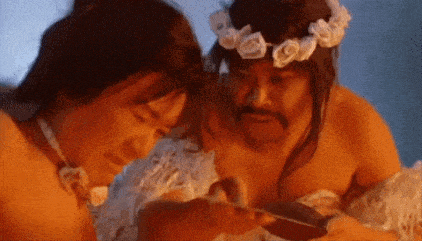 a man with a flower crown on his head is sitting next to a woman in a white dress .