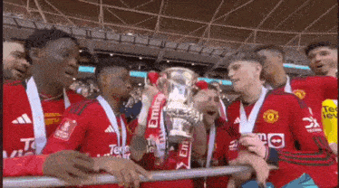 a group of young men in red jerseys are holding a trophy in a stadium .