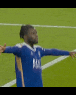 a soccer player in a blue shirt is standing on a soccer field with his arms outstretched .