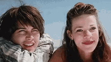 a boy and a girl are sitting next to each other on the beach and smiling .