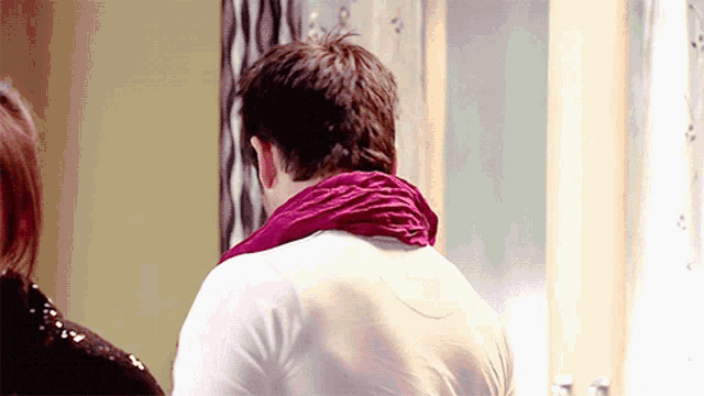 a man wearing a white shirt and a purple scarf around his neck looks over his shoulder