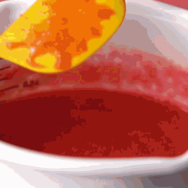 a yellow spatula is being used to stir a red liquid in a bowl