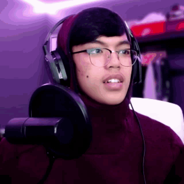 a young man wearing headphones and glasses is talking into a microphone .