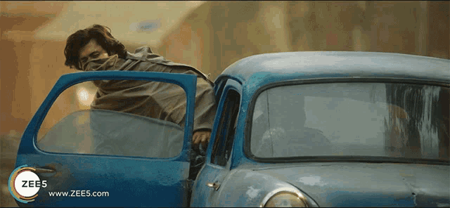 a man is getting out of a blue car with the website www.zees.com at the bottom