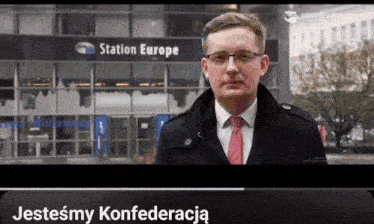 a man in a suit and tie stands in front of a building that says station europe