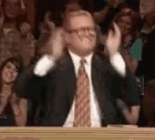 a man in a suit and tie is clapping in front of a crowd of people .