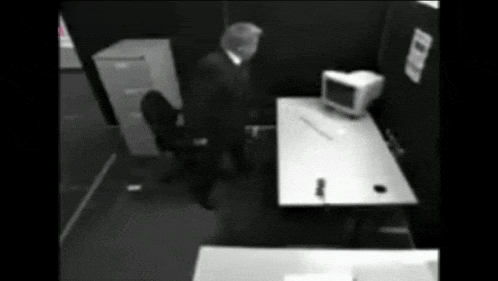 a black and white photo of a man standing in front of a desk