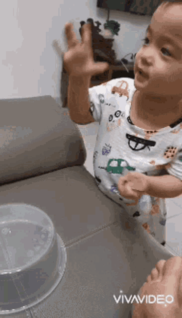 a baby is playing with a plastic container on a couch in a video taken by vivavideo