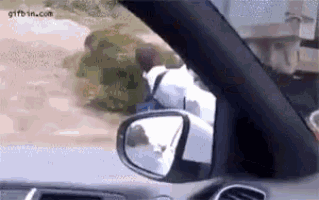 a car is driving down a dirt road and a person is standing in the grass .