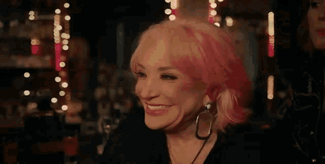 a woman with pink hair is laughing with her mouth open in a bar .