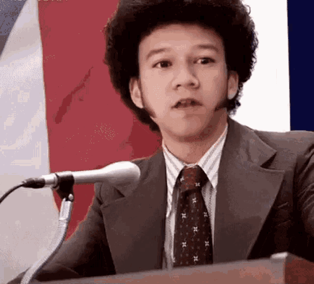 a man in a suit and tie is speaking into a microphone .