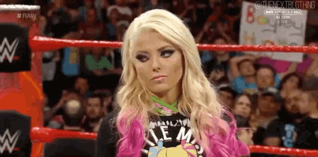 a woman with blonde hair and pink hair is standing in a boxing ring .