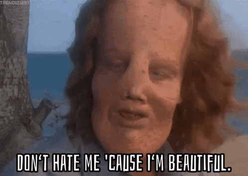 a man with red hair is standing on a beach and says `` don t hate me cause i 'm beautiful '' .
