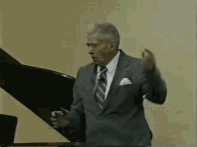 a man in a suit and tie is standing next to a piano .