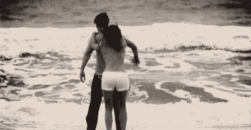 a man and a woman are hugging on the beach near the ocean .