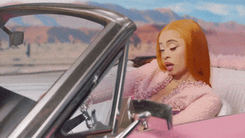 a woman with red hair is sitting in a pink convertible