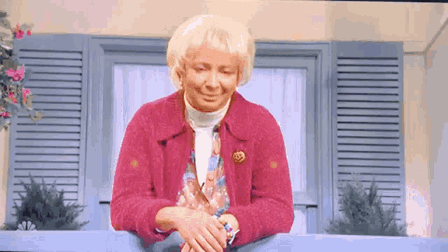 an elderly woman in a pink sweater is sitting on a window sill
