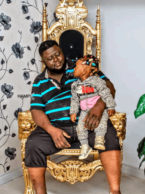 a man is sitting on a chair holding a little girl with the word hamp on the wall behind him