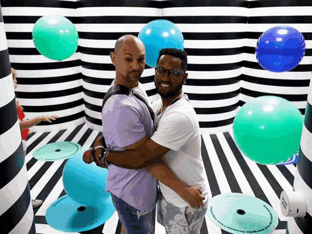 two men are hugging in a room with balloons and a sign that says " i love you "