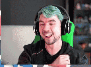 a man with green hair is wearing headphones and smiling while sitting in a chair .