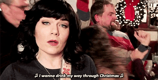 a woman singing i wanna drink my way through christmas in front of a group of people