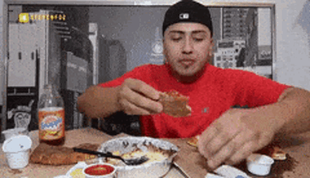 a man in a red shirt is eating a piece of pizza