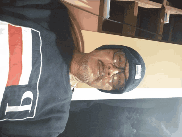 a man wearing a beanie and glasses is wearing a shirt with the letter t on it