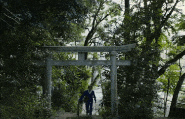 a man walking up a set of stairs under a torii gate with trees in the background