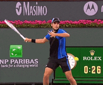 a tennis player is swinging a racket in front of a sign that says masimo