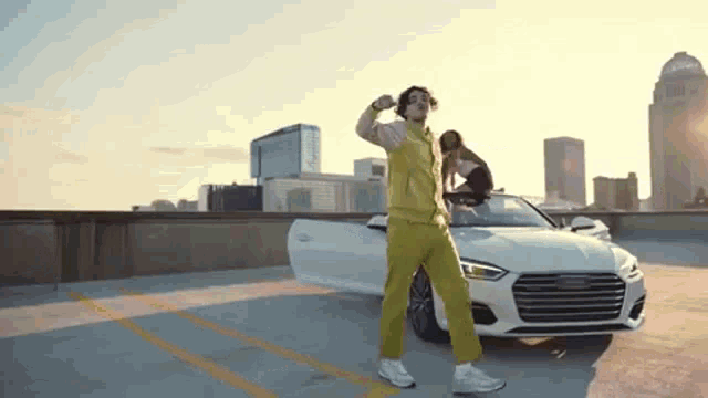 a man in yellow pants is dancing in front of a white car .