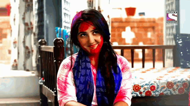 a woman with holi paint on her face is sitting on a bed in front of a sony television advertisement