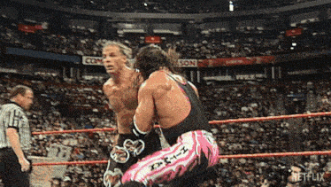 two wrestlers are fighting in a wrestling ring while a referee watches .