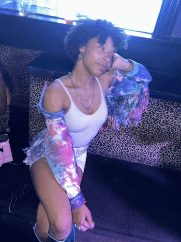 a woman in a white tank top and tie dye jacket is sitting on a leopard print couch