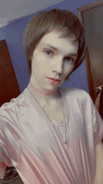 a young man wearing a choker necklace and a pink shirt takes a selfie