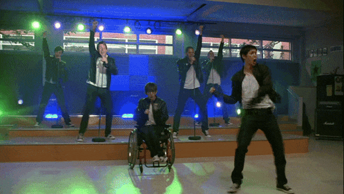 a man in a wheelchair sings into a microphone in front of a group of people on a stage