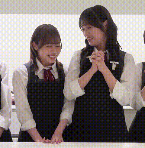 two girls in school uniforms are standing next to each other at a table and smiling .