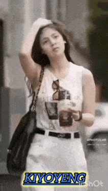 a woman wearing a white tank top and white pants is holding a cup of coffee and a black purse ..