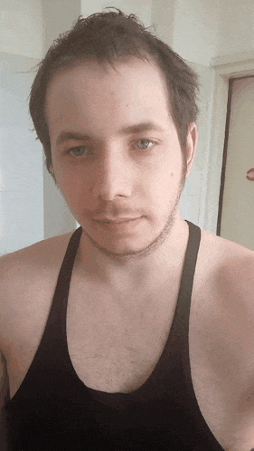 a man with a beard wearing a black tank top looks at the camera