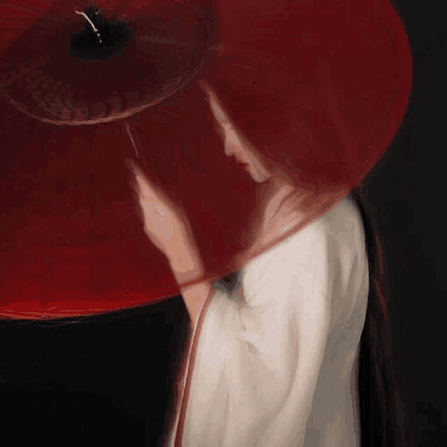 a woman in a white dress is holding a red umbrella in her hand .