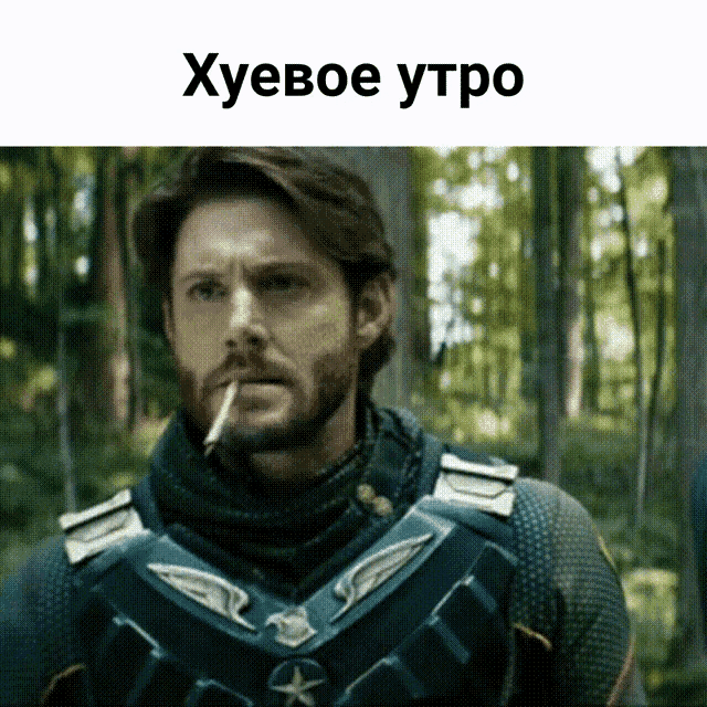 a man with a beard is smoking a cigarette in a forest and the caption says " хуевое утро "