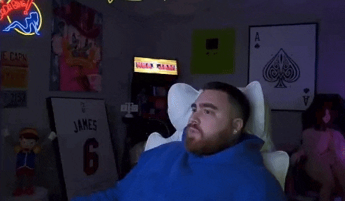 a man in a blue hoodie is sitting in a chair and holding his head .