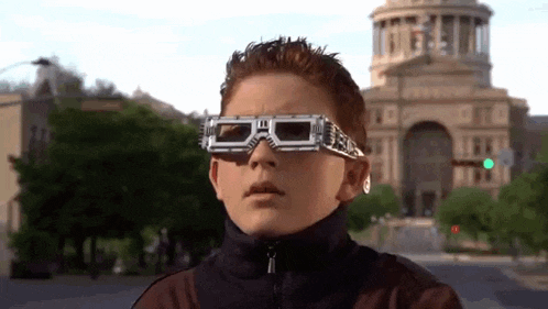 a young boy wearing a pair of 3d glasses is standing on a city street .