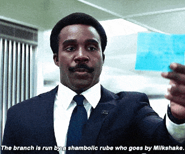 a man in a suit and tie is holding a piece of paper with the words the branch is run by a shambolic rube
