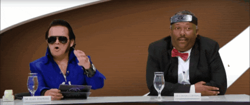 two men are sitting at a table and one has a name tag that says dr. elvis presley