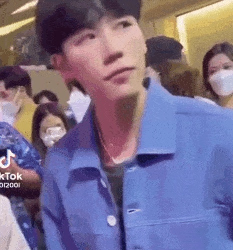 a young man in a blue jacket is standing in a crowd of people wearing masks .