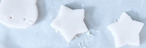 three pieces of white clay in the shape of a cat , a star , and a heart are sitting on a table .