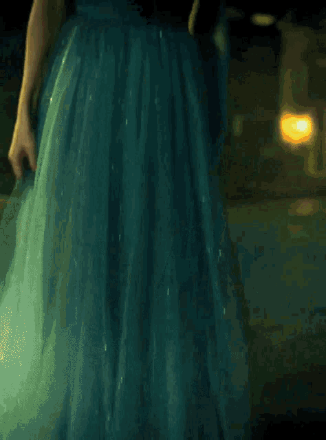 a woman in a blue dress with a plunging neckline is standing in a dark room